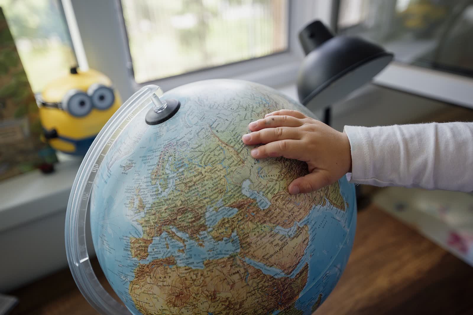 A child’s hand resting on a desk globe showing Europe and Africa
