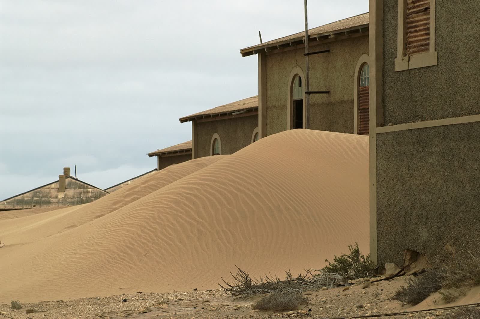 Abandoned houses in Kolmanskop, Namibia, half-buried by an advancing sand dune