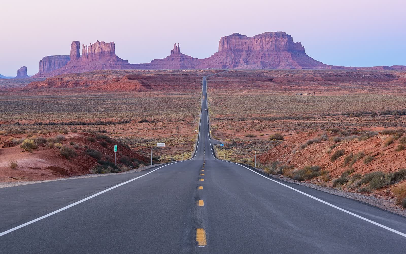 Long straight desert highway running toward the buttes of Monument Valley at dusk