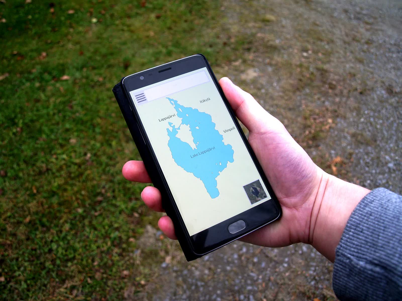 A hand holding a smartphone showing the outline of a mystery lake on a map
